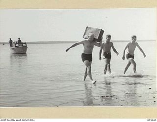 VOTING IN NORTH WEST AUSTRALIA. THE RETURNING OFFICER AND HIS ASSISTANT ARRIVING IN THEIR SWIMMING COSTUMES AT AN OUTPOST IN NORTH WEST AUSTRALIA TO ISSUE BALLOT PAPERS TO AUSTRALIAN TROOPS TO VOTE ..