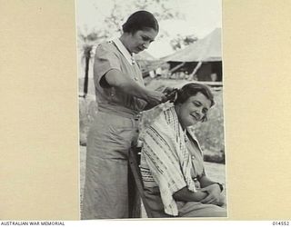 1943-04-01. AUSTRALIAN NURSES IN NEW GUINEA. UNDER THE SHADE OF A TREE. SISTER J. CRAMERI OF ARMADALE, VICTORIA, CUTS THE HAIR OF SISTER M. HOLDING OF MALVERN, VICTORIA. (NEGATIVE BY N. BROWN)