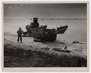 Photograph of a U.S. Marine Standing By a Wrecked Japanese Landing Barge