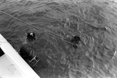 Crewmen from the salvage ship USS CONSERVER (ARS-39) position a tire in the water, as they prepare to begin salvage operations on a Coast Guard boat that sank when hurricane Iwa passed through the area