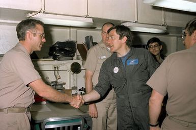 Secretary of the Navy John F. Lehman Jr., center, shakes hands during his visit aboard the aircraft carrier USS KITTY HAWK (CV-63)