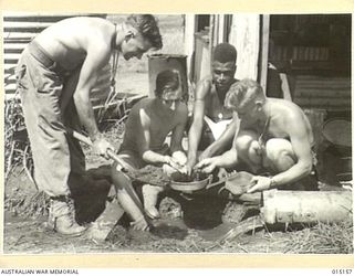 1943-06-29. NEW GUINEA. WAU-MUBO AREA. IN AN OFF MOMENT PTE. R. DAVIES, OF VIC., L/C ALLEN OF VICTORIA, AND PTE JOHN LUCAS, OF VIC., WITH FUZZY WUZZY NARRAMON EXAMINE THEIR IMPROVISED WASHING PANS ..