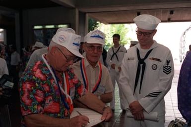 Stanley R. Mode, left, and Martin B. Bruns, center, describe "crossing-the-line" activities on the USS ARIZONA to their escort, Aerographer's Mate 1ST Class Mike Williams, at the USS ARIZONA Memorial Visitors Center following the 50th anniversary Remembrance Day ceremonies that honored them and other survivors of the Dec. 7, 1941, attack on Pearl Harbor