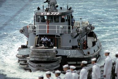 Sailors aboard the arriving amphibious command ship USS BLUE RIDGE (LCC-19) man the rail as the large harbor tug NOGALES (YTB-777) pulls alongside to assist the ship into the harbor