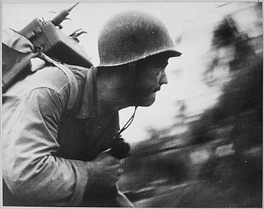 A US Marine charges across the beach on Peleliu Island, Palau Islands, the "walkie talkie" firmly strapped to his back and clutching a radio phone in his right hand.