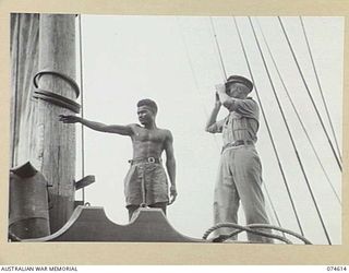 AT SEA. 1944-07. TX16092 LIEUTENANT H M MARKEY, 12TH SMALL SHIPS COMPANY, SKIPPER OF THE AK95 AND A NATIVE MEMBER OF THE CREW SCANNING THE HORIZON AS THE VESSEL APPROACHES LAE