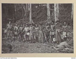 WONGINARA MISSION, NEW GUINEA. 1945-04-06. WARRANT OFFICER 2 JOHN BORRIT GODWIN, AUSTRALIAN NEW GUINEA ADMINISTRATIVE UNIT PATROL OFFICER (1), WITH MEMBERS OF THE 2/3 INFANTRY BATTALION AND NATIVE ..