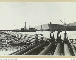 MILNE BAY, PAPUA, NEW GUINEA. 1944-04-03. THE PIPE LINES LEADING TO THE PIER AND A BERTHED TANKER DISCHARGING FUEL TO BULK STORAGE TANKS AT 2ND BULK PETROLEUM STORAGE COMPANY