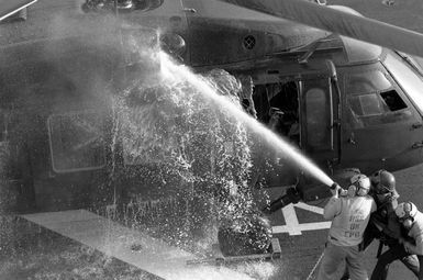 Flight deck crewmen hose down a UH-60 Blackhawk helicopter upon its landing aboard the amphibious assault ship USS GUAM (LPH 9) during Operation URGENT FURY. The helicopter's engine was hit by anti-aircraft fire on the island of Grenada