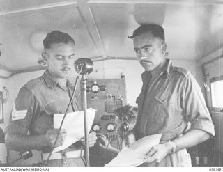 WEWAK, NEW GUINEA. 1945-10-29. SERGEANT N.S.W. BRAY (1) AND SERGEANT E.C. PARRANT (3) MEMBERS OF 1 BROADCASTING STATION, AUSTRALIAN ARMY AMENITIES SERVICE, AT THE MICROPHONE OF RADIO STATION 9AJ ..