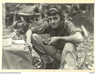 DANMAP RIVER AREA, NEW GUINEA. 1945-01-01. NX190531 GUNNER L.R. COUSINS, 2/3RD FIELD REGIMENT, OPERATING A RADIO SET FROM A FRONT LINE POSITION