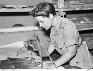 LAE, NEW GUINEA, 1945-05-23. SAPPER J.L. BAILEY, AWAS, PLOTTING POSITIONS FROM AERIAL PHOTOGRAPHS ONTO MAPS AND CHARTS AT FIRST ARMY SURVEY. AWAS PERSONNEL ARE AT LAE TO RELEASE MEN OF FIRST ARMY ..