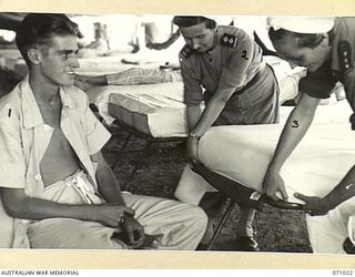 HELDSBACH MISSION, FINSCHHAFEN AREA, NEW GUINEA. 1944-03-13. VFX59385 SISTER L.G. RAE (2), AND NFX70247 SISTER R. FALLICK (3) MAKING THE BED OF N443665 PRIVATE SPENCER (1), IN A TENT WARD AT THE ..