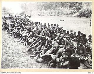 KIARIVU, NEW GUINEA, 1945-08-17. REFUGEE NATIVES LINED UP ON THE AIRSTRIP FOR COUNTING AND INSPECTION BY CAPTAIN R.R. COLE, THE ASSISTANT DISTRICT OFFICER, AUSTRALIAN NEW GUINEA ADMINISTRATIVE ..