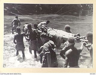 BOUGAINVILLE, 1945-05-18. PRIVATE J.W. BARRETT, B COMPANY, 57/60 INFANTRY BATTALION, BEING CARRIED BY NATIVES ACROSS A FAST FLOWING RIVER ON HIS WAY BACK TO AN ADVANCED DRESSING STATION. HE WAS ..
