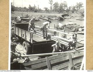 LAE, NEW GUINEA. 1944-06-14/02. TROOPS OF THE 12TH WATER TRANSPORT OPERATING COMPANY, UNLOADING IRRIGATION PIPES AT LAE FOR THE AUSTRALIAN FARM UNIT AT WAU. IN THE BACKGROUND CAN BE SEEN THE ..