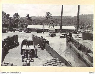 WEWAK BEACH, NEW GUINEA. 1945-10-18. MEMBERS OF 8 PORT OPERATING COMPANY LOADING STORES AND FUEL DRUMS ONTO A TRUCK FROM LANDING CRAFT, TANK FOR TRANSPORTATION TO STORES DUMPS. CONTROL TOWER AND ..