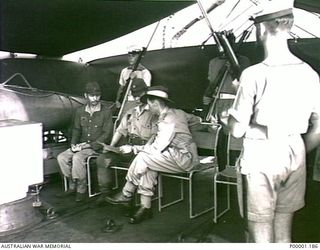 THE SOLOMON ISLANDS, 1945-08-20. AN AUSTRALIAN OFFICER ABOARD HMAS LITHGOW OFF MOILA POINT EXPLAINS SURRENDER PLANS TO TWO JAPANESE SERVICE PERSONNEL. (RNZAF OFFICIAL PHOTOGRAPH.)