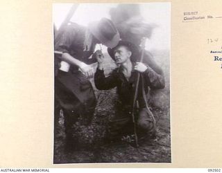 WEWAK AREA, NEW GUINEA, 1945-05-20. PTE C.I. BURFORD (1), LIGHTS A SMOKE FOR PTE K.J. LATIMORE (2), WHILE ADVANCING IN THE RAIN. THE MEN ARE MEMBERS OF 2/8 INFANTRY BATTALION