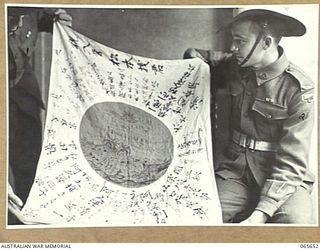 MELBOURNE, VIC. 1944-04-19. A JAPANESE FLAG CAPTURED BY MEMBERS OF THE 2/12TH INFANTRY BATTALION AT FINSCHHAFEN ON THE 2ND OCTOBER, 1943, DISPLAYED BY GUNNER PARKER, LEFT (1) AND GUNNER TOWNSEN (2)