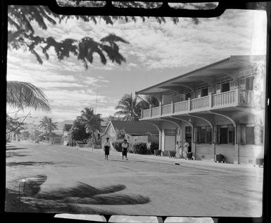 Two Fijians walking down a street past [Northern Hotels?] in Lautoka, Fiji