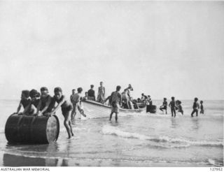 LAKEKAMU RIVER, PAPUA. 1942-07. NATIVES UNLOAD CARGO FOR KANGA FORCE FROM THE "ROYAL ENDEAVOUR" AT THE MOUTH OF THE RIVER, WHERE A SAND SPIT HAS BARRED THE ENTRANCE. SUPPLIES WILL BE MOVED BY CANOE ..