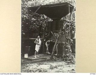PERSONNEL OF NO. 5 PLATOON (PIONEERS), HEADQUARTERS COMPANY, 27TH INFANTRY BATTALION WASHING UNDER THE INGENIOUS SHOWER SYSTEM BUILT BY MEMBERS OF THE UNIT. THIS SYSTEM WAS MADE BY INVERTING AN ..