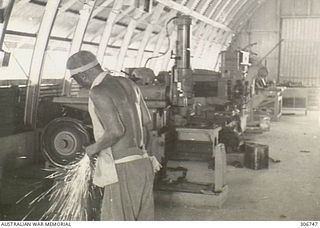 Sparks fly from a lathe used by a bare-chested Japanese prisoner held at the RAN War Criminal Compound at an RAN shore base, as he prepares tools in the machine shop at the compound. Work on this ..