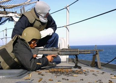 US Navy (USN) GUNNER's Mate Second Class (GM2) Benjamin Clark (background), observes as USN Photographer's Mate Second Class (PH2) Herbert Banks, fires a 7.62 mm M60 general purpose machine gun, during weapons qualifications aboard the USN Wasp Class Amphibious Assault Ship USS SAIPAN (LHA 2), while the ship is underway conducting training in the Atlantic Ocean