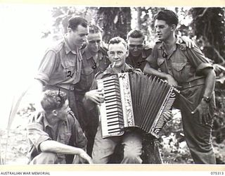 NAGADA, NEW GUINEA. 1944-08-16. PERSONNEL OF E TROOP, 22ND BATTERY, 106TH TANK ATTACK REGIMENT JOIN IN A SING-SONG AROUND A PIANO ACCORDION PLAYER DURING ONE OF THE UNIT STAND DOWN PERIODS. ..