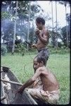 Canoe-building: men use lengths of vine to lash outrigger frame to a canoe