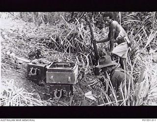 MAPRIK, NEW GUINEA. C.1946. IN THE FIELD, A MEMBER OF THE FRONT LINE BROADCASTING UNIT, FAR EASTERN LIAISON OFFICE, OPERATES A BATTERY POWERED FIELD AMPLIFIER UNIT WATCHED BY A NEW GUINEA NATIVE, ..