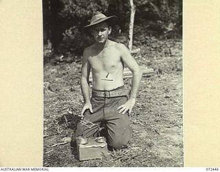 AMBOGA RIVER, NEW GUINEA. 1944-04-17. QX58352 SIGNALMAN O'BRIEN, 24TH LINE SECTION, 18TH LINES OF COMMUNICATION SIGNALS DISPLAYING TWO OF HIS ASH TRAYS AND MODEL AIRCRAFT CONSTRUCTED FROM BULLETS ..