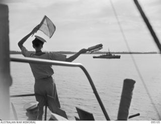 AT SEA, OFF BUIN, BOUGAINVILLE, 1945-08-20. A SIGNALLER ON BOARD THE CORVETTE HMAS LITHGOW USING SEMAPHORE TO PASS ON PROGRESS NEWS OF THE SURRENDER NEGOTIATIONS TO A CORVETTE WHICH PROVIDED ..