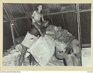 JACQUINOT BAY, NEW BRITAIN. 1945-04-26. PRIVATE J. HEEVEY (1), WATCHING TWO ANGAU NATIVE BOYS STACKING A RECORD LOAD OF MAIL AT 5 DIVISION AREA, 7 BASE POST OFFICE