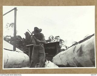 SOGERI, NEW GUINEA. 1943-11-20. A MEMBER OF THE STAFF OF THE SCHOOL OF SIGNALS, NEW GUINEA FORCE, STRIPPING BARK FROM A LOG A THE UNIT SAWMILL