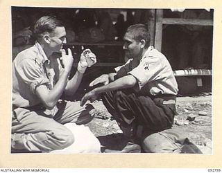 LAE, NEW GUINEA. 1945-06-09. CORPORAL R.A. SHEENS (1), EXCHANGES EXPERIENCES WITH SEPOY ALI, JAT BATTALION WHILE WAITING FOR AMBULANCE TRANSPORT TO THEM THEM TO THE HOSPITAL SHIP MANUNDA