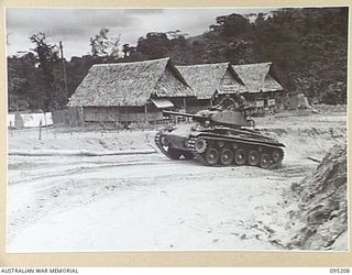 LARUMA RIVER, TOROKINA AREA, BOUGAINVILLE, 1945-08-14. AN M24 LIGHT TANK CLIMBS A ROAD PAST NATIVE STYLE BUILDINGS DURING TESTS CONDUCTED BY THE BRITISH WAR OFFICE TRIALS TEAM (TANKS)