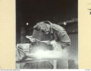 LABU POINT, LAE, NEW GUINEA. 1944-03-24. NX96559 CRAFTSMAN K. FORSYTH, IN THE ELECTRIC WELDING WORKSHOP AT THE 1ST WATERCRAFT WORKSHOP WORKING ON THE REPAIR OF LANDING BARGE PARTS