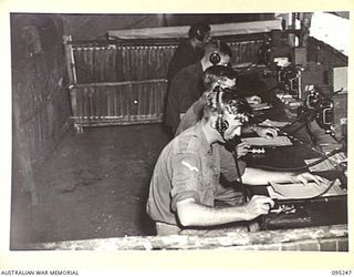 CAPE WOM, WEWAK AREA, NEW GUINEA, 1945-08-14. SIGNALMEN AT SIGNALS, 6 DIVISION RECEIVING MESSAGES ON WIRELESS RECEIVERS AND OPERATING TRANSMITTERS BY REMOTE CONTROL. THE TRANSMITTERS ARE ..