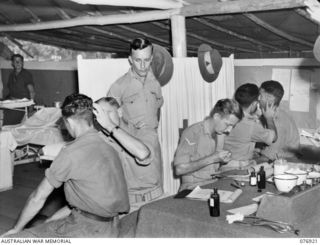 WX31556 Captain (Capt) H C Pope (2) and TX6484 Capt P Zerman (5), Medical Officers examining patients in the Regimental Aid Post of the 18th Australian Field Ambulance during the morning sick ..