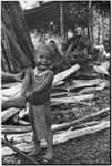 Pig festival, pig sacrifice, Tsembaga: smiling child stands by women preparing leaves to thatch sacrifice house