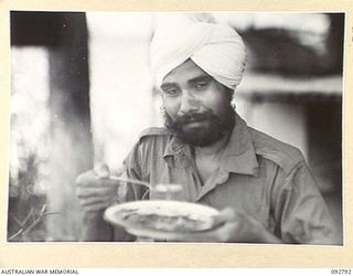 LAE, NEW GUINEA. 1945-06-09. AN INDIAN, A FORMER PRISONER OF WAR, NOW A 2/7 GENERAL HOSPITAL PATIENT, HAVING A MEAL BEFORE EMBARKING ON THE HOSPITAL SHIP MANUNDA