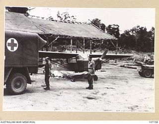 AITAPE, NEW GUINEA. TRANSFERRING A CASUALTY FROM THE AUSTER TO ROAD AMBULANCE FOR TRANSPORT TO HOSPITAL