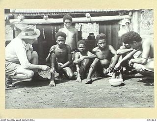 KOKODA, NEW GUINEA. 1944-04-13. P386 WARRANT OFFICER II, R. PRICE, SUB DISTRICT OFFICE, AUSTRALIAN NEW GUINEA ADMINISTRATIVE UNIT, WITH NATIVES WHO ARE AWAITING TREATMENT FOR TROPICAL ULCERS AT THE ..