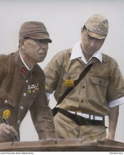 Lieutenant General Hatazo Adachi, Commander of the 18th Japanese Army in New Guinea, pen in hand, with a Japanese interpreter at the table holding the surrender document, during the formal ..