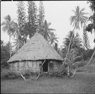 Circular grass hut with a statue at the doorway, New Caledonia, 1967 / Michael Terry