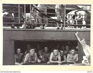 THE WHARF, JACQUINOT BAY, NEW BRITAIN, 1945-08-13. HEADQUARTERS 5 DIVISION TROOPS BILLETED IN THE HOLD GIVE A SMILING FAREWELL ON THE TROOPSHIP VAN OUTHOORN BEFORE SAILING FOR AUSTRALIA