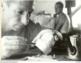 KILIGIA, NEW GUINEA. 1944-03-13. WX3649 SERGEANT M. KCKENNA, DENTAL MECHANIC, "E" SECTION, 2/5TH DENTAL UNIT, SETTING UP A SET OF DENTURES READY FOR TRYING IN THE PATIENT'S MOUTH. THE OBJECT OF ..