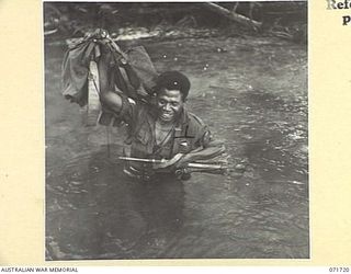 SINGORKAI - WEBBER POINT AREA, NEW GUINEA, 1944-03-21. SERGEANT CHARLES, A MEMBER OF "C" COMPANY, PAPUAN INFANTRY BATTALION, HOLDS EQUIPMENT ABOVE WATER WHILE CROSSING THE YIMBUNGE RIVER